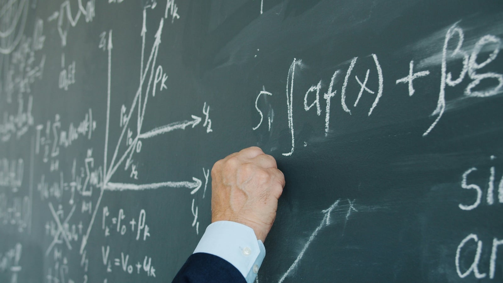 A teacher's hand writing calculus formulas on a chalkboard — integrals, summations, and 3D coordinate axes.